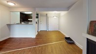 This single-floor residence offers a well-organized layout with distinct living, dining, kitchen, bedroom, and bathroom areas. The living room serves as the central gathering space, featuring wood-style flooring, a fireplace with a simple mantle, and a large sliding glass door fitted with vertical blinds that allow natural light to fill the room. A wall-mounted HVAC unit provides climate control near the patio access point.

The kitchen is positioned adjacent to the living and dining areas, accessible via a pass-through counter that also functions as a breakfast bar. It is outfitted with dark espresso-toned cabinetry, taupe countertops, a stainless steel sink, and a decorative tile backsplash in neutral tones. A white appliance suite completes the space.

The bedroom offers a comfortable, carpeted environment with a large window dressed in vertical blinds, providing natural light and outdoor views. The textured ceiling adds a subtle design element consistent throughout the unit.

The bathroom includes a white soaking tub, a vanity with dark cabinetry and taupe countertop, an integrated sink, and a large mirror. Wood-style flooring extends into this space, maintaining a cohesive aesthetic throughout the residence.