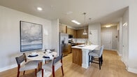 This single-floor, two-bedroom, two-bathroom residence offers a well-designed layout that balances comfort and functionality. Light wood-tone flooring flows throughout the main living areas, giving the space a warm and cohesive feel.

The open-concept kitchen is a standout feature, outfitted with wood-grain cabinetry extending to the ceiling, stainless steel appliances including a French door refrigerator and range, white quartz countertops, and a classic subway tile backsplash. A central island with pendant lighting provides additional prep space and seating. The adjacent dining area offers an intimate setting with recessed lighting and clean, neutral walls.

The living room is brightened by a large sliding glass door that invites natural light and provides outdoor views, complemented by light-filtering drapes and light wood flooring.

The primary bedroom is generously sized, featuring plush carpet, a ceiling fan, and direct access to a spacious walk-in closet with wire shelving systems. A second closet and full bathroom are also available for guests or additional occupants. Both bathrooms are finished with clean white tile surrounds and classic fixtures.

A dedicated in-unit laundry room with a full-size washer and dryer adds everyday convenience, completing this practical and stylish residence.