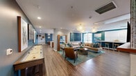 Located at 703 Baywood Dr in Petaluma, California, this thoughtfully designed amenity floor offers a sophisticated and welcoming environment for residents. The space is anchored by a stunning lounge and living area that immediately impresses with its bold teal accent walls, warm hardwood-style flooring, and an eye-catching arrangement of sculptural pendant chandeliers. Comfortable seating areas are thoughtfully arranged around a linear electric fireplace set into a tile-clad wall, complemented by a large mounted television — creating an ideal space for relaxation and social gatherings. A shuffleboard table and curated artwork add personality and depth to the room.

The combined kitchen and living room area is equally impressive, featuring stainless steel appliances, warm wood cabinetry, a textured accent wall, and an expansive waterfall-edge island with bar seating illuminated by globe pendant lights. The hallway connects the various areas with ease, accented by dramatic coral-inspired chandeliers that carry the design language throughout.

The dedicated exercise room is well-appointed with a full rack system, free weights, a punching bag, spinning bikes, and mirrored walls — all finished in the same vibrant teal palette. Outside, landscaped walkways, a gated courtyard, and covered parking complete this well-rounded residential amenity offering.