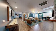 Located at 703 Baywood Dr in Petaluma, California, this thoughtfully designed amenity floor offers a sophisticated and welcoming environment for residents. The space is anchored by a stunning lounge and living area that immediately impresses with its bold teal accent walls, warm hardwood-style flooring, and an eye-catching arrangement of sculptural pendant chandeliers. Comfortable seating areas are thoughtfully arranged around a linear electric fireplace set into a tile-clad wall, complemented by a large mounted television — creating an ideal space for relaxation and social gatherings. A shuffleboard table and curated artwork add personality and depth to the room.

The combined kitchen and living room area is equally impressive, featuring stainless steel appliances, warm wood cabinetry, a textured accent wall, and an expansive waterfall-edge island with bar seating illuminated by globe pendant lights. The hallway connects the various areas with ease, accented by dramatic coral-inspired chandeliers that carry the design language throughout.

The dedicated exercise room is well-appointed with a full rack system, free weights, a punching bag, spinning bikes, and mirrored walls — all finished in the same vibrant teal palette. Outside, landscaped walkways, a gated courtyard, and covered parking complete this well-rounded residential amenity offering.