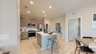 This thoughtfully designed single-floor residence offers a cohesive blend of modern aesthetics and functional living. The open-concept kitchen is a standout feature, outfitted with flat-panel wood-tone cabinetry, white quartz countertops, a subway tile backsplash, and a full suite of stainless steel appliances. A central island with bar seating provides additional workspace and a casual dining option, while light wood-look flooring flows seamlessly throughout the space. The adjacent dining area offers an intimate setting with ample natural light and direct sightlines to the living spaces. The living room makes a bold design statement with a deep navy accent wall, ceiling fan, and large windows that allow natural light to fill the room. The bedrooms are serene and comfortable, each equipped with ceiling fans, generous windows, and access to walk-in closets featuring wire shelving systems. The primary en-suite bathroom is elegantly finished with wood-tone vanity cabinetry, white quartz countertops, a frameless glass walk-in shower with large-format tile, and light wood-look tile flooring that extends the home's cohesive palette. Recessed lighting throughout ensures a bright, welcoming ambiance in every room.