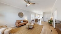 This single-story, 2-bedroom, 2-bathroom home offers a thoughtfully designed open-concept layout that maximizes functionality and flow. Light hardwood-style flooring runs throughout the main living areas, complementing the neutral, soft grey walls and crown molding details that give the space a clean, polished feel.

The combined living and dining area is bright and welcoming, featuring a ceiling fan with a wood-toned finish, large windows with white blinds that allow generous natural light, and ample room for both relaxing and entertaining. The kitchen is a well-equipped galley-style space outfitted with crisp white cabinetry, white quartz countertops, stainless steel appliances — including a refrigerator, electric range, microwave, and dishwasher — and a rear door providing additional natural light.

The primary bedroom is a comfortable retreat with carpeted flooring, a window with blinds, crown molding, and direct access to a spacious walk-in closet featuring wire shelving systems. Both bathrooms are finished in clean white tones, with one featuring a full tub-shower combination. A dedicated in-unit laundry area houses a full-size washer and dryer. The home is completed by a hallway connecting all rooms efficiently, making the layout practical for everyday living.