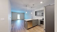 Located at 1015 Gant Hill Drive in Brentwood, Tennessee, this well-appointed one-bedroom, one-bathroom residence offers a thoughtfully designed single-floor layout with modern finishes throughout. The open-concept kitchen and living area serves as the heart of the home, featuring light wood-look flooring, recessed lighting, and a stylish peninsula with a white quartz countertop, undermount sink, and stainless steel dishwasher. Pendant lights hang above the peninsula, adding a contemporary touch. The kitchen is outfitted with gray shaker-style cabinetry, a marble-look tile backsplash, and a full suite of stainless steel appliances, including a range, over-the-range microwave, and refrigerator. The adjoining living area is bright and open, with neutral walls and access to a private exterior door that allows natural light to flow in. The bedroom offers a comfortable retreat with plush carpet flooring, a ceiling fan, and a window overlooking the outdoors. The full bathroom includes gray vanity cabinetry, a white quartz countertop, a large mirror with overhead lighting, tile flooring, and a soaking tub. A walk-in closet with wire shelving completes the private quarters, providing ample storage in this clean, contemporary Brentwood residence.