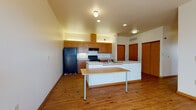 This single-floor unit at 1915 N 38th St in Milwaukee, Wisconsin offers a well-organized layout with consistent hardwood-style flooring flowing throughout. The open kitchen serves as the heart of the space, featuring warm-toned wood cabinetry extending to the ceiling, black appliances including a refrigerator and electric range, light countertops, and a peninsula with an integrated sink. Recessed and flush-mount lighting illuminates the kitchen and living area, which benefits from generous ceiling height, giving the space an open, airy feel.

Multiple rooms branch off from the central living area, each finished with the same hardwood-style flooring, neutral walls, and large windows that invite abundant natural light and outdoor views of the surrounding neighborhood. One room is equipped with a ceiling fan for added comfort.

The unit includes two bathrooms: one featuring a vanity with wood cabinetry and a grab bar for accessibility support, and another fully accessible bathroom with safety grab bars, a fold-down shower bench, and a wider layout. A dedicated laundry area houses a full-size washer and dryer beneath a countertop, accompanied by built-in shelving and a hanging rod for added storage and convenience.