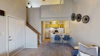 This two-story residence at Trails of Sunbrook in Saint Charles, Missouri offers a well-organized layout across two levels. The main floor centers around a carpeted living room with vaulted ceilings, a large window that draws in natural light, and a ceiling fan overhead. The open sightline connects the living area to the kitchen, which features warm wood-toned cabinetry, a range, refrigerator, microwave, and a peninsula breakfast bar with seating — ideal for casual dining. The kitchen is finished with light hardwood-style flooring, adding contrast to the carpeted living spaces. A staircase with a wood railing leads to the upper level, where the bedroom takes on a distinctive loft character. Sloped ceilings follow the roofline, creating an intimate atmosphere, while windows on multiple walls provide natural light and ventilation. The bedroom includes a mirrored sliding closet and ample space for a dresser and additional furnishings. The bathroom features a tiled tub and shower combination in neutral tones. Throughout the home, a soft, neutral color palette of warm grays and whites creates a calm, cohesive ambiance. The two-level design of this Trails of Sunbrook residence provides a functional and comfortable living environment in the heart of Saint Charles.