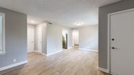 This single-floor residence showcases a clean, updated interior with a cohesive neutral color palette of soft grays and crisp white trim throughout. The open living and dining areas are finished with wood-look luxury vinyl plank flooring, offering a warm yet low-maintenance aesthetic. Large windows fitted with blinds allow natural light to filter through the main living spaces, creating a bright and welcoming atmosphere.

The kitchen stands out as a highlight of the home, featuring white shaker-style cabinetry, a white subway tile backsplash, a stainless steel sink, and a full suite of stainless steel appliances including a refrigerator, range, and over-the-range microwave. The light-toned flooring carries through into the kitchen, maintaining visual continuity.

The bedroom is carpeted for comfort and includes a ceiling fan with light fixture and a window that brings in natural light. Textured ceilings are present throughout the home, adding a classic residential feel.

The bathroom is neatly appointed with a white vanity, wood-look vinyl flooring, and a tub-shower combination with white subway tile surround. Multiple interior doors lead to closets and additional rooms, providing ample storage. The layout flows logically, making efficient use of the available space across the single floor.