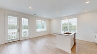 This single-floor residence in Lawrenceville, Georgia offers a thoughtfully designed layout with modern finishes throughout. The open-concept kitchen and living area is a central highlight, featuring light wood-style flooring, recessed lighting, and an abundance of natural light streaming through multiple large windows with blinds. The kitchen is equipped with stainless steel appliances, white shaker cabinetry with gold-toned hardware, a granite-topped island with an integrated sink, and generous counter space along the wall. A glass-paned door leads directly to a private balcony, offering scenic views of the surrounding wooded landscape. The bedrooms are carpeted for comfort and include ample closet space, with at least one walk-in closet fitted with wire shelving systems for organized storage. Each bedroom benefits from large windows that invite natural light and tree-lined views. The bathroom is clean and well-appointed, featuring a granite vanity with white cabinetry, gold hardware accents, a tub-shower combination with a glass enclosure, and wood-style flooring that ties the space together. A connecting hallway with smooth white panel doors provides access to the various rooms. The overall aesthetic is bright, clean, and contemporary, creating a welcoming and functional living environment.