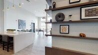 Located at 165 Belmont Ave in Belleville, NJ, this single-floor community amenity space is designed with a modern, open-concept layout that promotes both socializing and relaxation. Soaring double-height ceilings and an abundance of large windows flood the interior with natural light, creating an airy and welcoming atmosphere throughout.

The main lounge area features multiple distinct seating zones, including a comfortable sitting area with upholstered armchairs and sofas accented by bold artwork, as well as high-top bistro tables paired with vibrant rust-colored stools beneath colorful abstract paintings. A ping-pong table anchors the central game area, adding a recreational focal point to the expansive open floor plan.

A stylish reception-style counter with floating dark wood shelves and textured wall panels serves as an elegant divider within the space. The kitchenette is equipped with stainless steel appliances, a sink, dark wood cabinetry, a herringbone tile backsplash, and open shelving — ideal for entertaining or casual use.

Floor-to-ceiling windows along the terrace-facing wall provide sweeping outdoor views, with bar-height seating positioned to take full advantage of the scenery. Light wood-tone flooring runs throughout, tying together the cohesive, contemporary design of this well-appointed communal space.