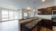 Located in Spokane Valley, WA, this single-floor unit offers a well-designed open-concept layout that seamlessly connects the kitchen, dining, and living areas. The kitchen is a standout feature, showcasing rich dark wood cabinetry extending to the ceiling for ample storage, a white subway tile backsplash, and dark granite countertops. A peninsula with an undermount sink and pendant lighting above serves as both a functional workspace and a natural division between the kitchen and living areas. Stainless steel appliances, including a refrigerator, range, microwave, and dishwasher, complete the kitchen.

Wood-style flooring runs throughout the main living areas, contributing to a warm, cohesive aesthetic. The living area is generously sized, featuring large windows and a glass door that opens to a private balcony, bringing in abundant natural light and outdoor views. A chandelier adds a refined touch to the dining space.

The bedrooms are carpeted for comfort and include closet space. The bathroom features a tub-shower combination and wood-style flooring. A dedicated laundry area accommodates a full-size washer and dryer. Overall, the space presents a clean, modern ambiance suited for comfortable everyday living.