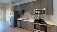 Located at 5050 Wayzata Blvd in Golden Valley, Minnesota, this contemporary single-floor residence showcases a thoughtfully designed interior with clean lines and modern finishes throughout. The open kitchen is a standout feature, equipped with a full suite of stainless steel appliances including a refrigerator with ice maker, range, microwave, and dishwasher. Rich wood-tone cabinetry extends floor to ceiling, complemented by a neutral subway tile backsplash and bright white countertops, creating a sleek and functional cooking space. Hardwood-style flooring flows seamlessly throughout the main living areas, lending warmth and continuity to the open layout. The spacious living area is bathed in natural light, courtesy of large sliding glass doors that lead to a private balcony overlooking lush outdoor greenery. The bathroom is well-appointed with wood-grain tile flooring, a full soaking tub and shower combination, a wood-tone vanity with integrated sink, and built-in shelving for added storage. An organized utility closet with built-in shelving provides practical storage solutions. The unit also includes an in-unit washer and dryer, as seen in the dollhouse view. Overall, the space presents a refined, modern aesthetic well-suited for comfortable urban living in the Golden Valley area.