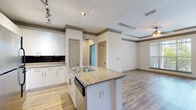 Located at 2910 Clairmont Rd in Atlanta, GA, this single-floor residence offers a well-designed open-concept layout that seamlessly connects the kitchen and living areas. The kitchen is a standout feature, equipped with stainless steel appliances, crisp white cabinetry, a dark subway tile backsplash, granite countertops, and a central island with a built-in sink and dishwasher. Track lighting and recessed fixtures illuminate the space effectively. The living area is distinguished by a tray ceiling with crown molding, a ceiling fan, and large windows that frame views of surrounding greenery, filling the room with natural light. Durable hardwood-style flooring runs throughout the main living spaces, while plush carpeting adds comfort to the bedroom. The bedroom benefits from its own ceiling fan and a generously sized walk-in closet outfitted with multi-level wire shelving. The bathroom features tile flooring, a tub-shower combination with tiled surround, granite-topped vanity, and a framed mirror. A dedicated laundry area with an in-unit washer provides added convenience. The overall ambiance is clean, bright, and modern, offering a functional and comfortable living environment.