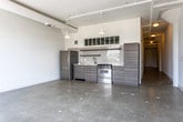 Located in Atlanta, GA, this single-floor loft showcases an industrial-modern aesthetic throughout. Polished concrete floors and soaring ceilings set the tone across the open-plan living area, which is bathed in natural light from large multi-pane windows offering treetop views. Exposed ductwork and track lighting add an authentic industrial character to the bright, white-walled interior.

The kitchen is thoughtfully outfitted with flat-front wood-grain cabinetry, white subway tile backsplash, light stone countertops, a stainless steel refrigerator, a gas range, and a single-basin sink — all complemented by a transom window above that draws in additional light. The open layout allows the kitchen to flow seamlessly into the expansive living area.

The space includes a well-proportioned bedroom with high ceilings and an interior transom window, alongside a generous walk-in closet equipped with wire shelving and hanging rods. Two bathrooms mirror the kitchen's modern design language, featuring wood-grain vanities with dark countertops, subway tile walls, large-format dark floor tile, open shelving, and a full bathtub with shower in the primary bath. This loft combines urban edge with practical, well-designed finishes throughout.