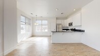 This well-designed 2-bedroom, 1-bathroom single-floor unit offers a clean, modern aesthetic defined by crisp white walls, light wood-style flooring, and an abundance of natural light throughout. The open-concept kitchen and living area forms the heart of the home, where a sleek kitchen is outfitted with white shaker cabinetry, dark countertops, stainless steel appliances — including a refrigerator, range, microwave, and dishwasher — and a peninsula that provides additional workspace and seating. Large windows in the living area flood the space with natural light and offer views of the surrounding urban streetscape. The primary bedroom is a comfortable, well-proportioned room featuring soft carpeting, a generous closet with a hanging rod, and a window with city views. The second bedroom also features carpeted flooring and a window with urban views, offering a bright and functional space. The shared full bathroom is finished in a clean, all-white palette with a tub/shower combo and wood-style tile flooring. A dedicated in-unit laundry area accommodates a full-size front-loading washer and dryer. A private balcony accessible from the living area adds an outdoor extension to this thoughtfully laid-out home.