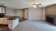 This single-floor residence offers a practical and comfortable layout designed for everyday living. The entryway opens directly into the main living area, which features warm neutral-toned walls, plush carpeting, a ceiling fan with a light kit, and a tiled fireplace framed by a large window that invites natural light into the space. The hard-surface flooring in the entryway transitions seamlessly into the kitchen and dining area.

The kitchen is well-equipped with white cabinetry featuring glass-front upper panels, a dark tile backsplash, track lighting, and white appliances including a refrigerator, electric range, and microwave. A peninsula with a dark countertop and an inset sink adds prep space and doubles as a casual dining or serving area, connecting the kitchen to the living space in an open, flowing layout.

The bedrooms are carpeted and finished with the same warm neutral palette, each featuring a ceiling fan with a light fixture and ample wall space. One bedroom benefits from a window with natural light, enhancing the room's airy feel.

The bathroom is clean and functional, offering a full soaking tub and shower combination, a white vanity with a dark countertop, and wood-look hard-surface flooring. Towel bars and built-in shelving provide convenient storage. Textured ceilings throughout the residence add a consistent finishing touch to the overall design.