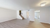 This two-story residence offers a clean, neutral aesthetic throughout, with design choices that prioritize functionality and versatility. The main level features wood-look plank flooring that extends through the open living areas, complemented by textured ceilings and crisp white walls. A spacious living room receives natural light through a large front-facing window, while a separate room at the rear opens directly to a private outdoor patio via sliding glass doors, providing views of mature palm trees and a fenced exterior space. The kitchen is outfitted with white cabinetry, speckled countertops, and white appliances including a refrigerator and electric range. A half bathroom on the main level offers a single vanity with wood-look flooring. A carpeted staircase leads to the upper level, where bedrooms feature plush carpet flooring and windows that bring in natural light. The primary bedroom includes access to an en-suite bathroom with a vanity, ample cabinetry, and a walk-in closet. Additional bathrooms are well-appointed with white vanities, speckled countertops, tub-shower combinations, and wood-look flooring, maintaining a consistent and cohesive finish throughout the home.