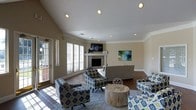 Located in Denton, Texas, this single-story home offers a well-designed living space centered around a bright and welcoming living room. The room immediately draws attention with its vaulted ceiling, which lends a sense of openness and grandeur to the space. Recessed lighting complements the natural light that flows in through multiple windows dressed with white horizontal blinds, illuminating the neutral-toned walls and hardwood flooring throughout.

A tiled fireplace serves as the focal point of the living area, framed by a clean white mantel and topped with a wall-mounted flat-screen television — a practical and stylish arrangement. Crown molding adds a refined architectural detail along the upper walls, enhancing the overall polish of the interior.

The living room is furnished with an eclectic yet cohesive mix of patterned accent chairs and a sofa in blue, green, and gold tones, arranged around a rustic wooden drum coffee table atop a light area rug. A piece of colorful abstract wall art adds a vibrant touch to the otherwise neutral palette. A side entry door with sidelights brings in additional natural light, further brightening this comfortable and thoughtfully appointed single-floor home.