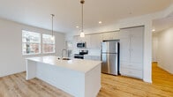This single-floor residence is designed with a clean, contemporary aesthetic, characterized by crisp white walls, light hardwood-style flooring in the main living areas, and an abundance of natural light. The open-concept kitchen serves as a central highlight, featuring a generous white quartz island with an integrated sink, sleek flat-front white cabinetry extending to the ceiling, stainless steel appliances including a refrigerator, electric range, and microwave, and pendant lighting suspended above the island. Large windows flood the kitchen and adjacent living areas with natural light and provide views of the surrounding neighborhood.

A long, well-lit hallway connects the main living areas to the private rooms, which are carpeted for comfort and include sliding closet doors for storage. One room features a corner window configuration, maximizing natural light intake. The bathroom is cleanly finished with a full tub-shower combination, chrome fixtures, and a grab bar for added accessibility. A dedicated laundry room houses a full-size GE washer and dryer. Throughout the unit, recessed lighting and flush-mount fixtures ensure consistent illumination, while the cohesive neutral palette creates a calm, move-in-ready atmosphere.