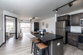 Located at 21 W Jefferson St in Waterloo, Iowa, this modern one-bedroom, one-bathroom unit offers a well-designed layout across a single floor. The open-concept living and kitchen area serves as the heart of the space, where light wood-tone flooring, crisp white walls, and track lighting create a clean, contemporary atmosphere. The kitchen is outfitted with rich dark wood cabinetry, stainless steel appliances including a refrigerator, range, microwave, and dishwasher, and a dark-topped island with bar seating — ideal for casual dining or meal prep. The living area flows seamlessly from the kitchen and opens to a private balcony through sliding glass doors, bringing in natural light and outdoor views of the surrounding Waterloo cityscape. The bedroom is a calm, well-proportioned retreat featuring a large window with city views, light flooring, and a built-in closet with dark panel doors. The bathroom continues the modern aesthetic with dark cabinetry, a single-sink vanity, and wood-look flooring. Additional conveniences include in-unit laundry, a utility room, and two closets, ensuring practical storage throughout. The unit's cohesive design and efficient use of space make it a functional and stylish urban residence.