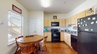 This single-floor residence offers a well-organized and functional layout spread across several rooms. A standout feature throughout the home is the rich, stained concrete flooring, which lends a warm, earthy character to every space.

The kitchen is thoughtfully designed with light maple cabinetry that extends to the ceiling, providing ample storage. Black appliances — including an electric range, built-in microwave, and dishwasher — anchor the cooking space, complemented by neutral countertops. A window allows natural light to filter in, and the adjacent dining area comfortably accommodates a round wooden table with chairs, making it ideal for casual meals.

The living room is an inviting, open space featuring tall walls and a large flat-screen TV as its focal point, paired with a comfortable sofa and a low coffee table. The room's clean, light-colored walls contribute to an airy and relaxed atmosphere.

The bedrooms are well-proportioned, each with windows and distinct character. One bedroom features a dedicated workspace setup, while another showcases a bold decorative wall tapestry, adding a personalized touch.

The bathroom is neatly appointed with light maple cabinetry, a wide vanity with an integrated sink, and a large mirror, maintaining the cohesive design language found throughout the home.