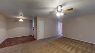 This single-floor unit offers a practical and functional layout connecting several distinct living spaces. The main living area is generously sized, featuring neutral beige walls, a textured ceiling, and a ceiling fan with integrated lighting. Carpet covers the living area floors, transitioning to wood-style flooring in the adjoining dining and kitchen zones. A sliding glass door fitted with vertical blinds admits natural light and provides exterior access.

The kitchen is efficiently arranged with white cabinetry, dark granite-style countertops, a white electric coil range with overhead ventilation, and a standard sink. Ample cabinet storage lines the walls, keeping the space organized.

The bedrooms continue the carpeted flooring and neutral color palette, each featuring a ceiling fan, window with blinds for natural light, and access to closet space. The textured ceilings carry throughout the unit, maintaining a consistent aesthetic.

The bathrooms are equipped with white cabinetry topped with dark countertops, tub-shower combinations with white tile surrounds, and wood-style flooring. The overall ambiance of the unit is clean and straightforward, offering a comfortable and move-in-ready environment.