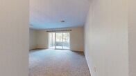 This single-floor residence offers a well-organized layout designed for comfortable everyday living. The main living area is generously proportioned, featuring soft carpeting underfoot and a wall of sliding glass doors that open directly onto an outdoor patio, flooding the space with natural light and providing pleasant views of the surrounding greenery. A chandelier accent near the dining transition adds a touch of warmth to the open layout, which flows seamlessly into the adjoining areas via hardwood-style flooring.

The kitchen is arranged in a practical U-shaped configuration, outfitted with warm honey-toned wood cabinetry, tile backsplash, light countertops, a corner stainless steel sink, and a dishwasher. Ample upper and lower cabinet storage makes this kitchen as functional as it is inviting.

The bedrooms are carpeted and bright, with large windows that bring in generous amounts of natural light and offer views of lush outdoor surroundings. The space includes two bathrooms: one featuring a white vanity, mirror, and a tub-shower combination, and a second with warm wood cabinetry and a glass-enclosed stand-up shower. Both are finished in neutral tones for a clean, timeless look throughout.