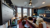 This single-floor space presents a cohesive, urban-inspired aesthetic that blends modern functionality with rich, layered design. The open-concept living area and kitchen serve as the heart of the unit, where large multi-pane windows flood the space with natural light and offer views of the surrounding cityscape. Linen drape panels frame the windows, complementing the warm hardwood flooring that runs throughout the main area. A ceiling fan anchors the living space, which features a tan leather sofa, a bold Persian-style rug in deep reds, and faceted geometric side tables that add sculptural interest.

The kitchen is outfitted with floor-to-ceiling dark cabinetry accented by brushed gold hardware, a dark tile backsplash, and stainless steel appliances, including a full-size refrigerator, range, and microwave. A modular black shelving unit along one wall provides additional storage and display space for the living area.

The bedroom offers a cozy retreat, featuring carpet flooring, an articulating black wall-mounted lighting system, a leather-framed bed dressed in rich burgundy and gold accents, and a curated gallery wall of framed artwork. The bathroom includes a dark stone-topped vanity with an undermount sink, brushed gold fixtures, and a large framed mirror, rounding out a space designed with careful attention to detail.