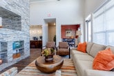This thoughtfully designed single-story space combines functionality with refined aesthetics across several distinct areas. The reception zone serves as the central hub, anchored by a dramatic floor-to-ceiling stacked stone column that draws the eye upward toward soaring vaulted ceilings with exposed wood beams and white shiplap detailing. The reception desk features elegant glass mosaic tile paneling, complementing the rich wood-look plank flooring and large-format hexagonal tile that defines the entry zone.

The entry vestibule welcomes visitors through full-height glass doors, transitioning into the main area via a geometric hexagonal tile floor in neutral tones. A warm-toned wood accent wall adds visual depth near a seating alcove with stylish chairs.

The adjacent lounge area is bathed in natural light from oversized windows that frame exterior views, and is furnished with comfortable seating in warm earth tones. A separate dining nook with pendant lighting offers additional gathering space.

A sliding barn door off the reception area opens into a business center with workstations and pendant lighting. The refreshment station features rich wood cabinetry, a quartz countertop, a glass tile backsplash, a built-in beverage cooler, and a coffee station, rounding out the amenities of this polished, community-oriented space.