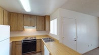 Located at 1617 Live Oak in Vista, unit #182 is an upstairs residence offering a practical, well-organized single-floor layout. The kitchen is a standout feature, equipped with warm oak cabinetry extending to the upper walls for generous storage, laminate countertops, a built-in electric range with overhead ventilation, a double-basin stainless steel sink, a white refrigerator, and a dishwasher. Tile flooring runs throughout the kitchen, and a window with vertical blinds allows natural light to fill the space. A peninsula counter connects the kitchen to the adjacent living area, which features plush carpeting, a textured ceiling, a sliding glass door opening to an outdoor space, and a wall-mounted air conditioning unit. A chandelier-style pendant light adds a decorative touch near the kitchen pass-through. The bedroom is generously proportioned with soft carpeting, a textured ceiling, a window with vertical blinds, and a sliding mirrored closet offering ample storage. The bathroom includes a wide oak vanity with a marbled countertop, a large mirror with a lighted fixture above, and a separate wet area with a full soaking tub, shower, and tile flooring.