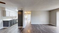 This single-story, 2-bedroom, 1-bathroom residence offers a thoughtfully designed layout with cohesive modern finishes throughout. Rich, dark wood-style laminate flooring flows through the open-concept living area and kitchen, while lighter wood-tone flooring carries into the bedrooms and closets, creating a warm and consistent aesthetic. The living room is a bright, open space anchored by a sliding glass door that invites natural light and opens to an outdoor area, complemented by a textured ceiling that adds subtle character. The galley-style kitchen is efficiently arranged with two-tone cabinetry — crisp white uppers paired with charcoal lower cabinets — white quartz countertops, a stainless steel sink, and stainless steel appliances including a refrigerator and range. A skylight above brightens the workspace considerably. The primary bedroom is generously sized, featuring two windows that bathe the room in natural light, and is accompanied by a spacious walk-in closet with dual hanging rods and shelving. The second bedroom also includes its own closet with a full-length hanging rod. The bathroom is finished with a wide quartz-topped vanity, gray cabinetry, and a large mirror. In-unit washer and dryer connections are visible within a dedicated closet space, adding everyday convenience.