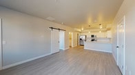 This thoughtfully designed single-floor unit offers a clean, modern aesthetic defined by neutral tones, light wood-style luxury vinyl plank flooring, and an open-concept layout that seamlessly connects the living area to the kitchen. The kitchen is a standout feature, outfitted with crisp white shaker cabinetry extending to the ceiling, white quartz countertops, a full suite of stainless steel appliances including a refrigerator with ice maker, electric range, built-in microwave, and dishwasher, as well as a peninsula with an undermount sink and pendant lighting above. The spacious living area is bright and airy, benefiting from natural light through multiple windows. A stylish sliding barn door with black hardware adds a contemporary touch and leads to additional rooms. The bedrooms are well-proportioned, each with windows offering exterior views and access to natural light. The bathroom features a full tub-shower combination, white vanity with ample storage, and black hardware accents that complement the overall design. A dedicated laundry area houses a stacked washer and dryer unit, providing added convenience. Throughout the unit, clean lines, consistent finishes, and a cohesive neutral palette create a welcoming and functional living environment.
