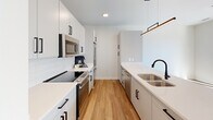 Located at 700 Semmes Ave in Richmond, Virginia, this thoughtfully designed one-bedroom, one-bathroom residence offers a clean, modern aesthetic throughout its efficiently utilized single-floor layout. Warm hardwood-style flooring runs continuously through the main living areas, complementing the crisp white walls and contemporary finishes that define the space.

The open-concept kitchen and living area serves as the heart of the home. The galley-style kitchen is outfitted with white flat-panel cabinetry accented by matte black hardware, a white quartz countertop, subway tile backsplash, stainless steel appliances, and a deep double-basin sink. A peninsula with built-in open shelving separates the kitchen from the living area, providing additional storage and a natural transition between spaces. Pendant lighting adds a polished finishing touch.

The bedroom is a bright, serene retreat featuring large sliding glass doors that open to a private balcony with views of the surrounding Richmond cityscape. A ceiling fan provides added comfort, and the room benefits from abundant natural light.

The bathroom is finished in a contemporary style with white subway tile surrounding the tub-shower combo, a sleek vanity with a white countertop and slate-blue cabinetry, matte black fixtures, and a large illuminated mirror. A dedicated laundry closet with a stacked full-size GE washer and dryer adds in-unit convenience.
