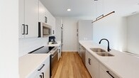 Located at 700 Semmes Ave in Richmond, Virginia, this thoughtfully designed one-bedroom, one-bathroom residence offers a clean, modern aesthetic throughout its efficiently utilized single-floor layout. Warm hardwood-style flooring runs continuously through the main living areas, complementing the crisp white walls and contemporary finishes that define the space.

The open-concept kitchen and living area serves as the heart of the home. The galley-style kitchen is outfitted with white flat-panel cabinetry accented by matte black hardware, a white quartz countertop, subway tile backsplash, stainless steel appliances, and a deep double-basin sink. A peninsula with built-in open shelving separates the kitchen from the living area, providing additional storage and a natural transition between spaces. Pendant lighting adds a polished finishing touch.

The bedroom is a bright, serene retreat featuring large sliding glass doors that open to a private balcony with views of the surrounding Richmond cityscape. A ceiling fan provides added comfort, and the room benefits from abundant natural light.

The bathroom is finished in a contemporary style with white subway tile surrounding the tub-shower combo, a sleek vanity with a white countertop and slate-blue cabinetry, matte black fixtures, and a large illuminated mirror. A dedicated laundry closet with a stacked full-size GE washer and dryer adds in-unit convenience.