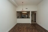 This well-appointed 2-bedroom, 2-bathroom single-floor residence offers a thoughtfully designed open-concept layout that maximizes both space and functionality. The interior is anchored by rich hardwood-style flooring that flows seamlessly throughout the main living areas, complementing the clean, modern aesthetic of the home.

The kitchen is a standout feature, showcasing sleek white cabinetry, dark contrast countertops, and a full suite of stainless steel appliances, including a refrigerator, range, and microwave. A breakfast bar peninsula provides both additional prep space and a natural dividing point between the kitchen and the adjacent living and dining areas. An elegant chandelier overhead adds a refined touch to the open dining space, enhancing the overall ambiance.

The bright, white walls and contemporary lighting fixtures throughout contribute to a crisp, airy atmosphere. Additional features include a frosted glass interior door that adds a charming architectural detail, along with visible ceiling vents that ensure comfortable climate control.

The two bedrooms offer comfortable retreats, while the two full bathrooms provide convenience for both residents and guests. The single-floor layout ensures easy, accessible living with a cohesive flow from room to room, making this a practical and stylish home.
