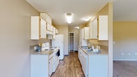 Located at 1012 Hidden Creek Dr NE in Keizer, Oregon, this single-floor, 2-bedroom, 2-bathroom home offers a well-organized layout with practical finishes throughout. The galley-style kitchen is a standout feature, lined with ample white cabinetry with light wood trim on both sides, providing generous storage and counter space. White appliances, including a range and refrigerator, complement the neutral-toned countertops and wood-look flooring that runs through the kitchen and main living areas. A hallway connects the kitchen to the rest of the home, leading to a walk-in closet area. Both bedrooms feature soft carpet flooring and neutral wall tones, creating a calm and comfortable atmosphere. The primary bedroom includes direct access to a bathroom, while large windows in the bedrooms frame views of surrounding greenery, filling the rooms with natural light. The bathrooms are finished with light countertops, white cabinetry, and a tub-shower combination with sliding glass doors. A vanity with a large mirror and built-in storage adds functionality. The overall design is clean and neutral, making each room versatile and move-in ready.