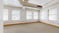 Located at 1003 Walnut St in the heart of Kansas City, MO, this two-bedroom, one-bathroom unit offers a well-designed single-floor layout with an urban loft character. The spacious primary bedroom is generously proportioned, featuring large windows with blinds that frame views of the surrounding downtown Kansas City skyline, allowing abundant natural light to fill the room. A ceiling fan adds both comfort and a functional touch to the space.

The secondary bedroom also benefits from multiple windows overlooking neighboring buildings, maintaining a bright and airy feel throughout. Warm-toned carpet flooring and distinctive orange baseboards run through the bedrooms and main living areas, providing a cohesive design element.

The open living and hallway area showcases the unit's industrial influences, with exposed spiral ductwork running along the ceiling and pendant lighting accenting the corridor. The kitchen features rich dark-wood cabinetry with a tile backsplash and white appliances, offering a contrast to the surrounding neutral palette.

The bathroom is finished with a dark wood vanity, a white countertop, a large mirror, and polished concrete flooring, giving it a clean and modern aesthetic. Natural wood doors throughout the unit add warmth to the overall design. This unit presents a compelling blend of industrial character and residential comfort in a vibrant urban setting.