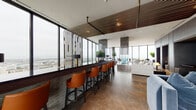 Located in the heart of downtown Oakland at 1314 Franklin St, this single-floor high-rise space delivers a striking blend of contemporary design and elevated functionality. Floor-to-ceiling curtain-wall glazing wraps much of the perimeter, framing sweeping panoramic views of the Oakland skyline, surrounding cityscape, and San Francisco Bay beyond, flooding the interior with abundant natural light throughout the day.

The open layout is thoughtfully organized into several distinct zones. A sleek bar counter lined with cognac leather barstools sits beneath a dramatic wood-slat ceiling detail with decorative pendant elements, creating a refined social focal point. Nearby, generous lounge seating areas feature deep upholstered sofas and leather accent chairs arranged to maximize the spectacular views, with large-format tile flooring throughout lending a clean, polished aesthetic.

A more intimate lounge corner incorporates a bold tufted amber wall panel with a wrap-around teal sectional sofa, offering a cozy, curated retreat. Elsewhere, built-in wall niches fitted with dark banquette seating and pendant lighting provide semi-private nooks ideal for smaller gatherings. Cylindrical architectural columns, textured wall cladding, and carefully selected greenery complete the sophisticated, cosmopolitan ambiance of this exceptional urban space.