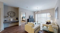 Located in Beavercreek, Ohio, this single-floor residence offers a thoughtfully designed open layout with contemporary finishes throughout. The living room serves as a central gathering space, showcasing rich hardwood-style flooring, a striking sputnik chandelier, and a large sliding glass door that floods the room with natural light and opens to an outdoor balcony view. The adjacent dining area features the same warm flooring and is accented by bold botanical wall art, creating a stylish transition between spaces. The kitchen is equipped with granite countertops, two-tone cabinetry in white and gray, a gray subway tile backsplash, black appliances, and a built-in wine rack, combining function with modern aesthetic. Both bedrooms are generously sized, carpeted for comfort, and brightened by large windows with exterior views. Each bedroom includes a ceiling fan and ample space for furnishings. The primary bedroom connects to a full en-suite bathroom featuring granite countertops, gray cabinetry, tile flooring, and access to a walk-in closet. A second bathroom offers a frameless glass-enclosed walk-in shower with neutral tile surrounds. Throughout the residence, a cohesive neutral color palette, quality materials, and modern lighting create a polished and inviting atmosphere.