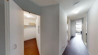 This efficient and thoughtfully laid-out one-bedroom, one-bathroom unit offers a comfortable single-floor living experience. The combined kitchen and living area forms the heart of the space, where light tile flooring in the kitchen transitions to rich, dark hardwood throughout the rest of the unit. The kitchen is equipped with stainless steel appliances, white cabinetry, and a dedicated pantry closet for additional storage. The open living area benefits from large windows that draw in natural light and offer views of the surrounding cityscape, creating a bright and inviting atmosphere. The textured ceiling adds a classic architectural detail consistent throughout the unit. The spacious primary bedroom comfortably accommodates a full bedroom suite and features its own large window with city views, continuing the dark hardwood flooring. A hallway connecting the main living areas provides access to two closets — one of which is a walk-in with built-in shelving and hanging rods — offering generous storage solutions. The bathroom is clean and functional, featuring a white vanity with a single sink, a mirrored medicine cabinet, and a shower-tub combination. Neutral gray walls throughout the unit provide a versatile backdrop suited to a variety of interior styles.