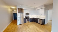 Located at 1885 N Milwaukee Ave in Chicago's vibrant Wicker Park neighborhood, this single-floor unit offers a thoughtfully designed open layout with modern finishes throughout. Light wood flooring flows seamlessly across the main living areas, complementing the neutral wall tones and creating a warm, cohesive aesthetic.

The kitchen is a standout feature, showcasing a two-tone design with dark lower cabinetry and crisp white upper cabinets extending to the ceiling for generous storage. A classic white subway tile backsplash pairs with white quartz-style countertops, while a full suite of stainless steel appliances—including a gas range, microwave, refrigerator, and dishwasher—provides a polished, functional workspace. Track lighting illuminates both the kitchen and open living area effectively.

The living space is generously proportioned, with large windows and a sliding glass door offering access to a private balcony and drawing in abundant natural light. Bedroom areas continue the light wood flooring and feature sizable windows with neighborhood views.

Bathrooms are finished with large-format dark floor tiles, white floating vanities, undermount sinks, and contemporary chrome fixtures. A dedicated in-unit laundry closet with a stacked washer and dryer adds everyday convenience. The overall design is clean, contemporary, and well-appointed.