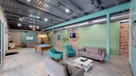 This single-floor clubroom blends industrial design with modern comfort, creating a dynamic and inviting communal space. The exposed ceiling showcases metal decking, steel beams, and visible ductwork, all illuminated by track lighting and a statement pendant fixture that add warmth and character to the room. Painted structural beams in a bold teal hue complement the mint-green accent walls, while exposed brick columns provide a rustic contrast that grounds the industrial aesthetic.

The space is divided into distinct functional zones. A recreation area features a classic wood-framed billiards table with a vibrant blue felt surface, perfect for casual gameplay and socializing. Adjacent to it, a well-appointed lounge area is furnished with a neutral-toned sofa, teal accent chairs, and a clean white coffee table, offering a comfortable setting for relaxed conversation or screen time. A wall-mounted flat-screen TV is positioned for easy viewing from the seating arrangement.

Light wood-toned flooring runs throughout, softening the industrial elements and tying the design together cohesively. The overall ambiance is energetic yet comfortable, making this clubroom an ideal gathering place.