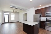 This single-floor unit offers a well-designed, open-concept layout that seamlessly connects the kitchen and living area. The kitchen is a standout feature, outfitted with rich dark-wood cabinetry, light quartz countertops, a full suite of stainless steel appliances including a refrigerator, electric range, microwave, and dishwasher, as well as a central island that provides additional prep and seating space. Open wall-mounted shelving adds a modern, industrial touch alongside the exposed metallic ductwork that runs across the ceiling, lending the space an urban loft aesthetic. Hardwood-style flooring flows throughout the entire unit, providing a warm, cohesive look. The living area is generously sized, illuminated by recessed lighting and a ceiling fan, with a main entry door flanked by windows that allow natural light to fill the space. The bedroom is comfortably proportioned, featuring its own ceiling fan and a window with an exterior view. A hallway connects the bedroom to the bathroom, which includes a vanity with shelving. A dedicated laundry closet houses a stacked Whirlpool washer and dryer, adding everyday convenience to this thoughtfully appointed unit.