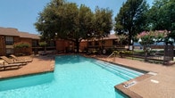Located at 1501 El Camino Real in Euless, Texas, this single-story property offers a well-appointed outdoor amenity area alongside thoughtfully designed interior spaces. The centerpiece of the outdoor area is a generously sized swimming pool with clearly marked depth indicators, surrounded by a wide concrete deck finished in warm earth tones. A covered wooden gazebo provides shaded seating, while additional lounge chairs are arranged poolside for relaxed outdoor enjoyment. Mature trees frame the perimeter of the pool area, offering natural shade and a sense of seclusion. A picnic table and safety equipment are also present, enhancing the functionality of the outdoor space.

The interior features wood-style plank flooring that adds warmth and a cohesive aesthetic throughout. Closet spaces are notably practical, featuring dual clothing rods and shelving along multiple walls, maximizing storage capacity. Textured ceilings and neutral gray wall tones create a calm, understated interior palette. The walk-in closets are well-lit and spacious, offering organized storage solutions. Overall, the property combines comfortable outdoor recreational amenities with practical interior features suited for everyday living.