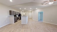 This well-appointed single-floor residence offers a thoughtfully designed open-concept layout that seamlessly connects the kitchen, dining, and living areas. The kitchen is a standout feature, showcasing sleek gray cabinetry, granite countertops, a central peninsula island, and a full suite of stainless steel appliances including a range, microwave, and refrigerator. Light wood-look vinyl plank flooring runs throughout the main living spaces, complementing the neutral warm-beige walls and recessed lighting overhead.

The spacious living area benefits from a ceiling fan with integrated lighting and an open flow that makes the space feel generous and airy. The bedrooms are finished with plush carpeting, ceiling fans, and natural light from windows with blinds. A walk-in closet with built-in shelving and hanging rods provides ample storage in the primary bedroom.

The bathrooms are finished with consistent granite-top vanities featuring dark cabinetry, tile flooring, and clean white fixtures. One bathroom includes a soaking tub and shower combination, while another features a dedicated walk-in shower. Throughout the home, a cohesive neutral palette and modern finishes create a clean, contemporary ambiance suited to a variety of lifestyles.