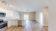 This well-appointed single-floor unit offers a thoughtfully designed open-concept layout that seamlessly connects the kitchen, dining, and living areas. The kitchen is a standout feature, showcasing crisp white shaker cabinetry, granite countertops, and a full suite of stainless steel appliances including a refrigerator with ice maker, range, over-the-range microwave, and dishwasher. A peninsula with a granite surface and an undermount sink provides additional workspace and casual dining potential, accented by elegant pendant lighting overhead. The open living area benefits from a ceiling fan with light kit and sliding glass doors that lead to a private balcony, filling the space with natural light and offering outdoor views. The bedrooms are generously proportioned, featuring warm hardwood-style flooring, neutral toned walls, and ample natural light from multiple windows. One bedroom provides direct access to a balcony through a glass door. A dedicated laundry area houses a stacked washer and dryer unit alongside a soaking tub and a window for natural ventilation. Throughout the unit, light wood-tone flooring, clean white trim, and warm beige walls create a cohesive, move-in-ready aesthetic suited for comfortable everyday living.