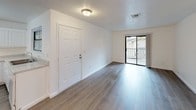 This single-floor unit is designed with a clean, functional layout that makes efficient use of its space. The main living area greets residents at the entry and features wood-look plank flooring throughout, crisp white walls, and a ceiling fan with a light fixture that provides both comfort and illumination. A sliding glass door at the far end of the living area fills the room with natural light and opens to a private balcony with views of the surrounding exterior. The kitchen is well-appointed with white cabinetry, light stone-look countertops, a double-basin stainless steel sink, and a full suite of white appliances including a refrigerator, electric range, and dishwasher. A window above the sink allows natural light into the space. The unit includes two bedrooms, each finished with plush carpet flooring, white walls, and windows that provide natural light and exterior views. The bathroom features tile flooring with a marble-style pattern and includes a full bathtub and shower combination, toilet, and towel bar. The 3D floor plan confirms a thoughtfully arranged layout connecting the kitchen, living area, bedrooms, and bathroom in a cohesive flow.