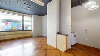 Located in the heart of Saint Paul, MN, this one-bedroom, one-bathroom unit at 2–26 Fourth St E offers a compact yet character-filled layout across a single floor. The living area immediately stands out with its eye-catching ornate tin ceiling, exposed ductwork lending an industrial edge, and warm terracotta-toned terrazzo tile flooring laid in a bold grid pattern that runs consistently throughout the entire unit. Large windows flood the main living space with natural light and frame views of the surrounding urban streetscape, including a colorful mural visible from outside.

The kitchen is efficiently arranged with light maple cabinetry, a dark countertop, a white range, and a full-size refrigerator. A peninsula-style counter provides a subtle division between the kitchen and the open living area. A pendant light fixture overhead adds a soft, functional glow to the cooking space.

The bedroom is a quiet, well-proportioned room with a window offering additional natural light and a baseboard heating unit. A double sliding-door closet provides ample storage.

The bathroom features a combined tub and shower, a toilet, and a single-sink vanity with light maple cabinetry and a framed mirror, maintaining the consistent warm aesthetic found throughout the unit. The terrazzo flooring continues seamlessly into this space, tying the entire unit together cohesively.