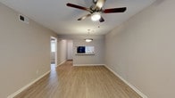 This single-floor residence offers a thoughtfully designed layout that balances open living areas with comfortable private spaces. The living and dining areas feature warm wood-look luxury vinyl flooring that extends throughout the main spaces, complemented by neutral gray-toned walls and clean white baseboards that create a bright, cohesive aesthetic. Ceiling fans are present throughout, providing both comfort and a consistent design element across rooms.

The kitchen is well-equipped with crisp white shaker-style cabinetry, granite-look countertops, a tile backsplash, and black appliances including a range and built-in microwave. A pass-through window connects the kitchen to the living area, enhancing the open feel of the shared spaces. An adjacent dining area features a pendant light fixture overhead.

The bedrooms are carpeted for added comfort, each equipped with a ceiling fan and window fitted with blinds that allow for natural light control. The rooms offer generous proportions suitable for a variety of furnishing arrangements.

The bathroom is finished with a granite-topped vanity, white cabinetry, wood-look flooring, and a full-size soaking tub with a shower. Overall, the space presents a clean, move-in-ready interior with consistent, modern finishes throughout.
