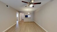 This single-floor residence offers a thoughtfully designed layout that balances open living areas with comfortable private spaces. The living and dining areas feature warm wood-look luxury vinyl flooring that extends throughout the main spaces, complemented by neutral gray-toned walls and clean white baseboards that create a bright, cohesive aesthetic. Ceiling fans are present throughout, providing both comfort and a consistent design element across rooms.

The kitchen is well-equipped with crisp white shaker-style cabinetry, granite-look countertops, a tile backsplash, and black appliances including a range and built-in microwave. A pass-through window connects the kitchen to the living area, enhancing the open feel of the shared spaces. An adjacent dining area features a pendant light fixture overhead.

The bedrooms are carpeted for added comfort, each equipped with a ceiling fan and window fitted with blinds that allow for natural light control. The rooms offer generous proportions suitable for a variety of furnishing arrangements.

The bathroom is finished with a granite-topped vanity, white cabinetry, wood-look flooring, and a full-size soaking tub with a shower. Overall, the space presents a clean, move-in-ready interior with consistent, modern finishes throughout.