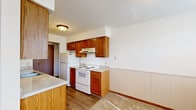 Located at 6255 Kenowa Ave SW in Grandville, Michigan, this single-floor residence offers three bedrooms, two bathrooms, and a practical layout designed for comfortable everyday living. The kitchen is efficiently arranged in a galley style, featuring warm wood cabinetry, light countertops, a double sink, a white electric range, and a refrigerator, all set atop durable hardwood-style flooring. A lower wainscoting detail adds a classic touch to the kitchen and adjoining areas. The living area is bright and open, with plush carpeting, white walls, and multiple windows that invite natural light into the space. The generously sized primary bedroom provides ample room and includes a built-in closet with shelving and hanging storage. The additional bedrooms are carpeted and well-proportioned, with closet access and windows that bring in natural light. One bedroom features a vaulted ceiling detail that adds architectural interest. The two bathrooms are clean and functional, with wood-toned vanities, speckled countertops, and wood-style flooring. Two hallways connect the layout efficiently. Overall, the space presents a warm, straightforward aesthetic with consistent wood accents and neutral tones throughout.