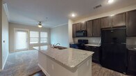 Located at 2574 S I-35 Frontage Rd in New Braunfels, Texas, this single-story unit offers a well-designed open-concept layout that connects the kitchen and living areas seamlessly. The kitchen serves as a central hub, anchored by a large island with granite countertops and a double-basin sink. Dark espresso cabinetry lines the walls, providing ample storage, while black appliances—including a refrigerator, range, and built-in microwave—complete the kitchen's cohesive aesthetic. Wood-look flooring runs throughout the kitchen, transitioning to plush carpeting in the living and bedroom areas.

The living area benefits from crown molding, a ceiling fan, and a glass door with an adjacent window that invites natural light and provides outdoor access. Multiple bedrooms feature carpeted floors, ceiling fans, and windows with blinds, offering comfortable, well-lit spaces. One bedroom includes access to a walk-in closet.

The unit includes two bathrooms, both finished with dark vanity cabinetry and granite-style countertops. One bathroom features a tiled tub-shower combination with wood-look flooring, while the other offers a similar layout with a natural light window. Throughout, neutral tones and consistent finishes create a cohesive and functional living environment.